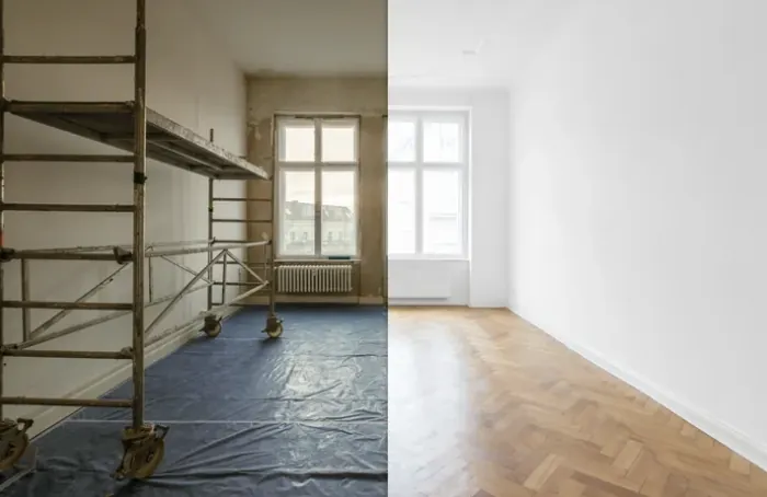 Empty room split between scaffolding and plastic sheeting on one side and clean white walls with herringbone floor on the other